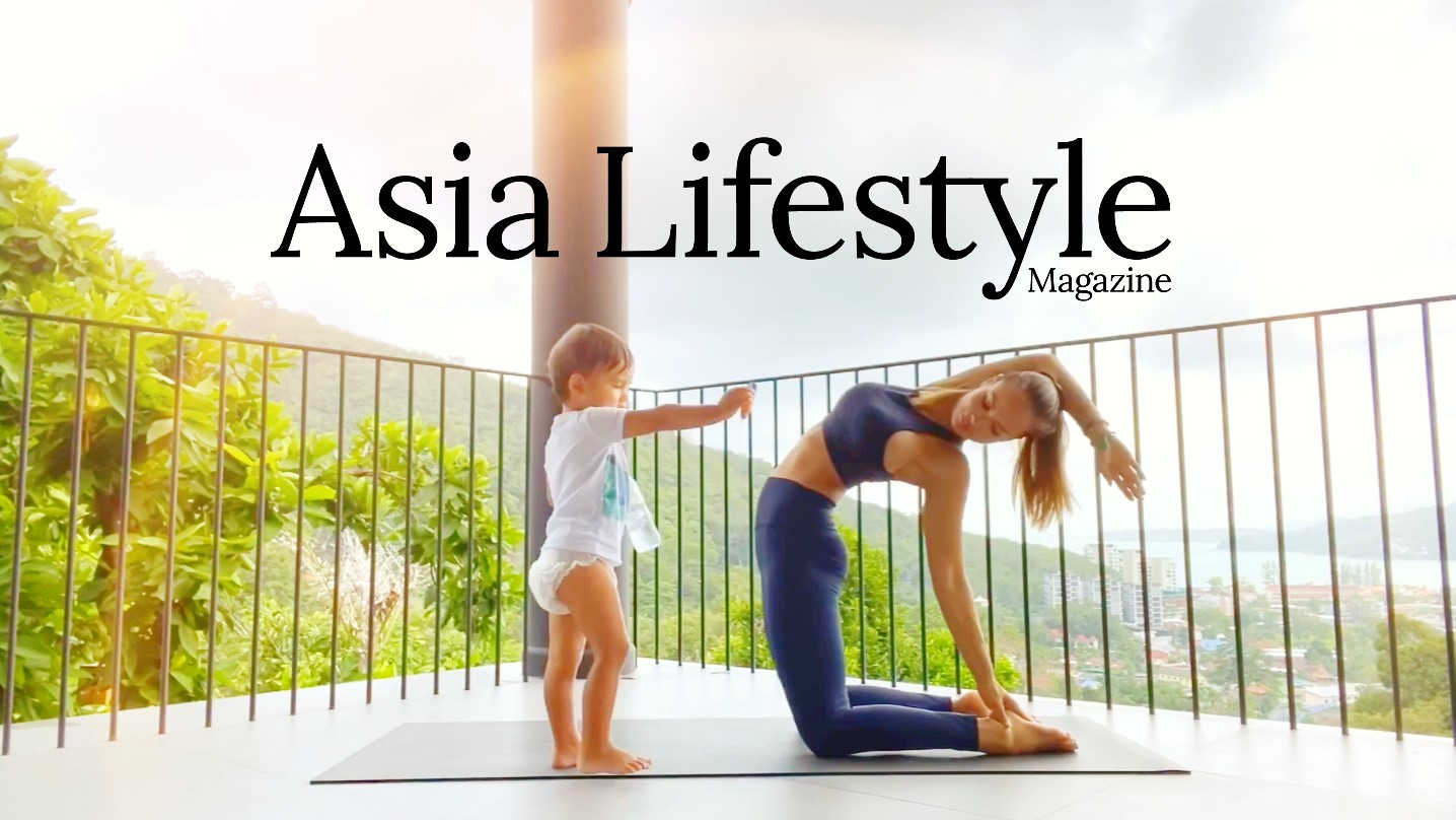 A woman in a yoga pose on a balcony mat while her toddler stands beside her