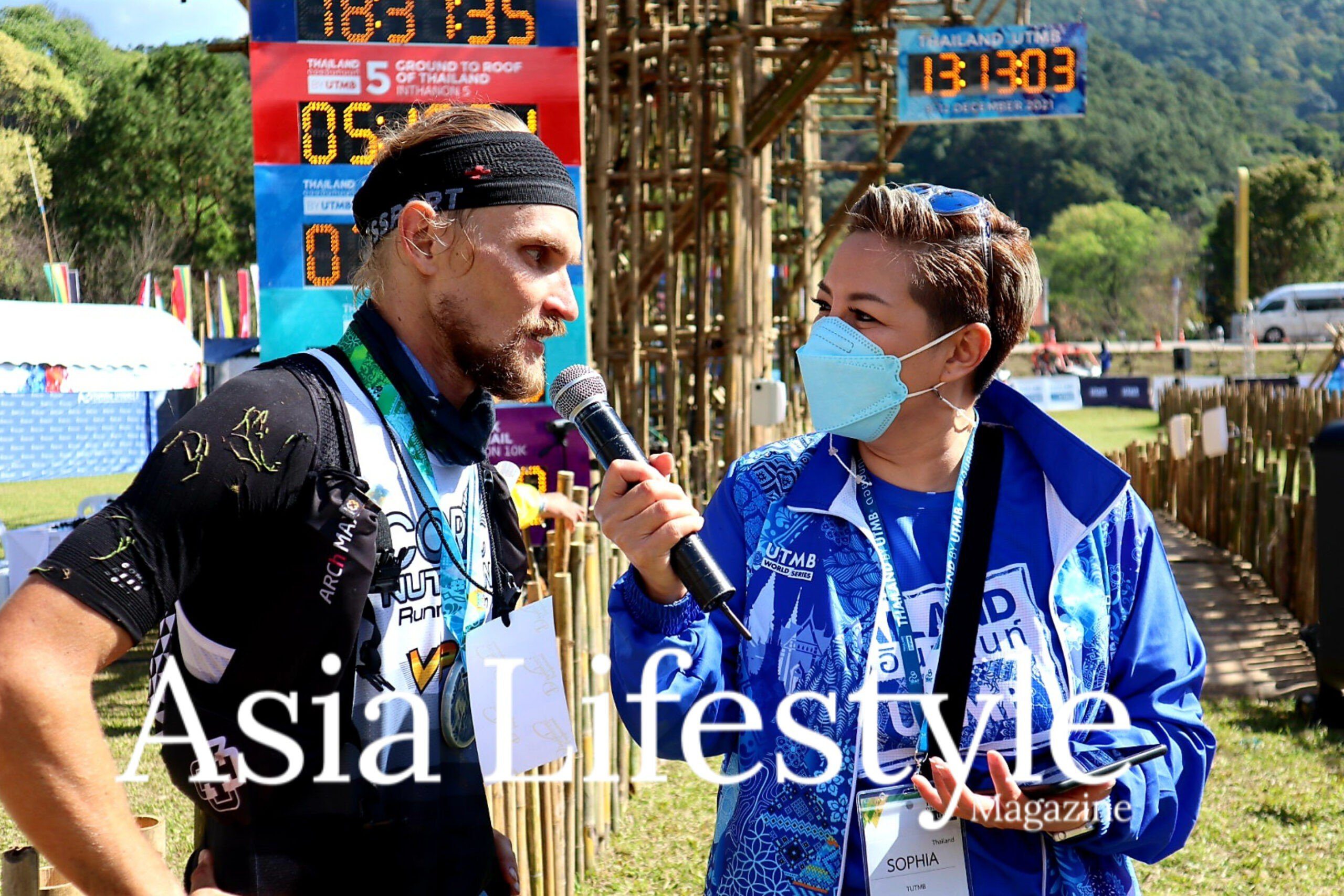 Serious Injury Doesn’t Stop Ivan Vlasenko at Thailand by UTMB A finisher with a race medal is interviewed beside the timing clock at a Thailand by UTMB trail race