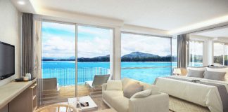 Thailand’s 2026 Condominium Launches: Key Insights for Property Investors and Foreign Buyers A condominium room with a bed and sofa opening through full-height glass to a bay and headlands