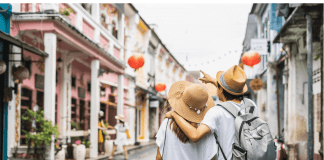 Two travellers with a backpack walk a Phuket Old Town street lined with pastel shophouses and red lanterns