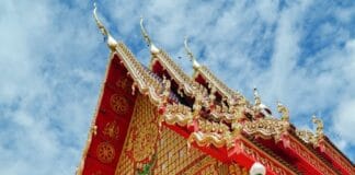 TAT Governor Interview An ornate red and gold Thai temple hall with gilded carving beneath a blue sky