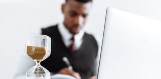 Oman Income Tax 2025: Essential Insights for Expats and Employers on the Gulf’s New Tax Reform An hourglass on a desk with sand running through, a man writing beside a laptop behind