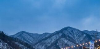 Families ice-fish through holes in a frozen river at a Korean winter festival, snow-covered mountains behind