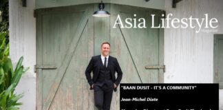 A man in a dark suit leans against weathered green barn doors, with caption text naming Jean-Michel Dixte of Baan Dusit Thani