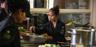 Chefs in black uniforms prepare vegetables in a busy professional kitchen