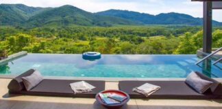 Infinity pool on a villa terrace with cushions along the edge, looking out over forested hills