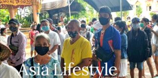 A queue of masked people waiting at an outdoor food distribution point in Thailand during the pandemic