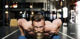 A bearded man performs a press-up on dumbbells in a gym