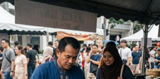 A Thai chef cooks pad thai in a wok at a Thailand Fest stall in Kuala Lumpur as a customer watches