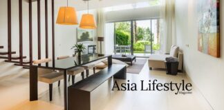 Open-plan living and dining room of a modern villa, with a long dark wood table and glass doors onto a garden terrace