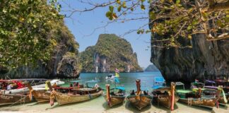 Longtail boats moored on a white sand beach between limestone karst cliffs in southern Thailand