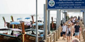 Revitalizing Thailand Tourism: Bold Moves on the Horizon A Thai marine officer briefs tourists on a pier beneath a Sustainable Tourism Zone sign, longtail boats moored behind