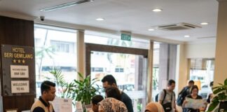 “Domestic Tourism Soars: RM34 Billion in 1Q2026!” Guests check in at a Malaysian hotel reception desk, a family with luggage waiting behind