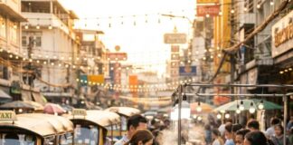 Ho Chi Minh City vs Bangkok: A Comprehensive Comparison of Two Vibrant Destinations A photographer crouches to shoot a street-food cart on a busy Bangkok street lined with tuk-tuks