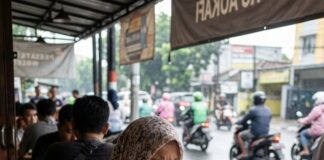 Indonesia’s Social Media Crackdown: What It Means for Kids Under 16 An Indonesian student in a headscarf and school uniform uses her phone at a roadside cafe table