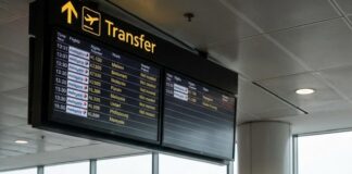 “Malaysia Airlines: Kuala Lumpur’s Next Aviation Gem?” A traveller with a backpack looks up at a Transfer board at Kuala Lumpur airport, a Malaysia Airlines jet outside