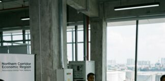 A Malaysian official briefs reporters beside a Northern Corridor Economic Region display, oil storage tanks outside