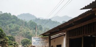 Mekong to Sea: Discover Your Riverside-to-Beachside Adventure! A cycle tourer pauses outside a roadside homestay in Laos as a woman tends a cooking pot over a fire