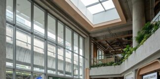 “Retail Sector Reimagined: Unveiling a New Growth Phase” A man works on a laptop at a mezzanine counter in a modern food hall, a train passing the window behind