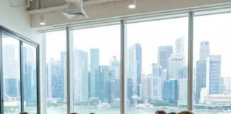 A team works at laptops around a long table in a Singapore office overlooking the Marina Bay skyline
