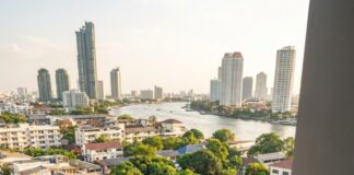 Southeast Asia Expat Community Outgrowing Dubai: What You Need to Know About the Shift and Its Impact A woman works at a laptop and tablet on a high-rise balcony overlooking the Chao Phraya river in Bangkok