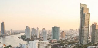 A group raises wine glasses on a Bangkok rooftop terrace at sunset, the Chao Phraya river behind them