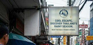 Thailand Summer Escape: The European Dream Getaway A traveller walks a wet Bangkok pavement past food carts beneath a tourism billboard promoting the rainy season