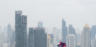 Soaring High: Wingsuit Flight Adventures in Bangkok A wingsuit flyer descends over central Bangkok as onlookers watch from a rooftop terrace, the Grand Palace below