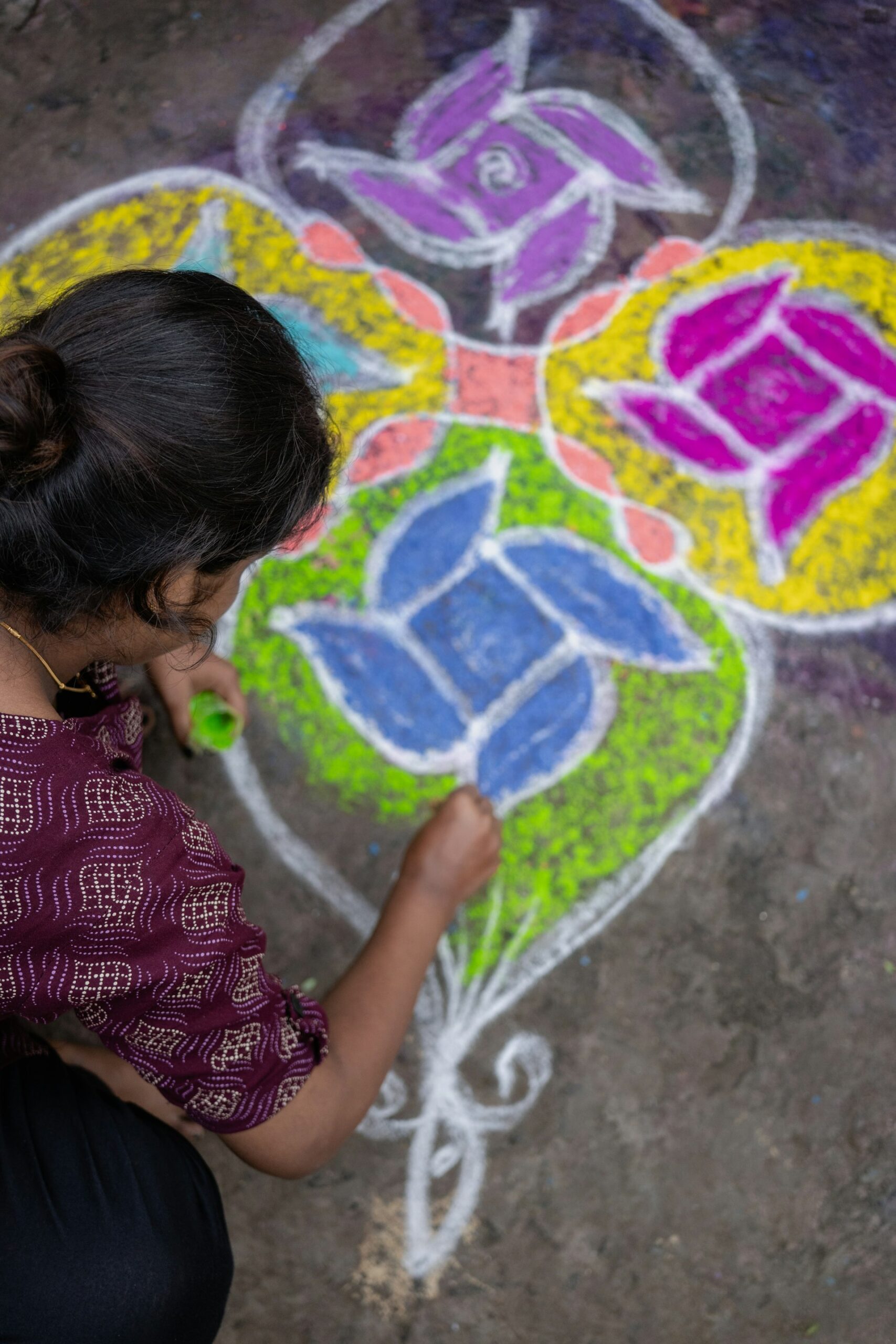 Woman drawing a kolam style floor design by hand at a doorstep