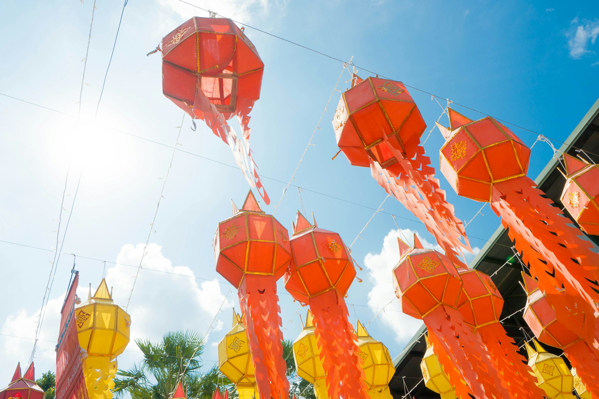 Red and yellow Lanna style lanterns hanging against a blue sky in northern Thailand