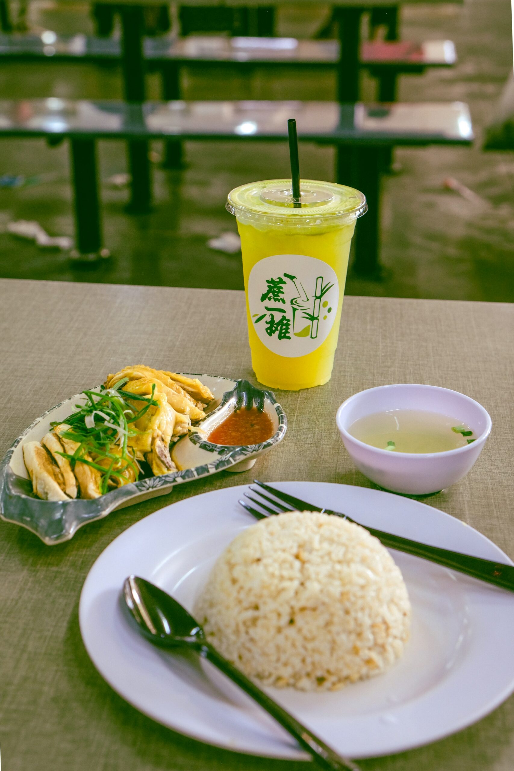 Plate of Hainanese chicken rice with a cup of sugarcane juice at a hawker table