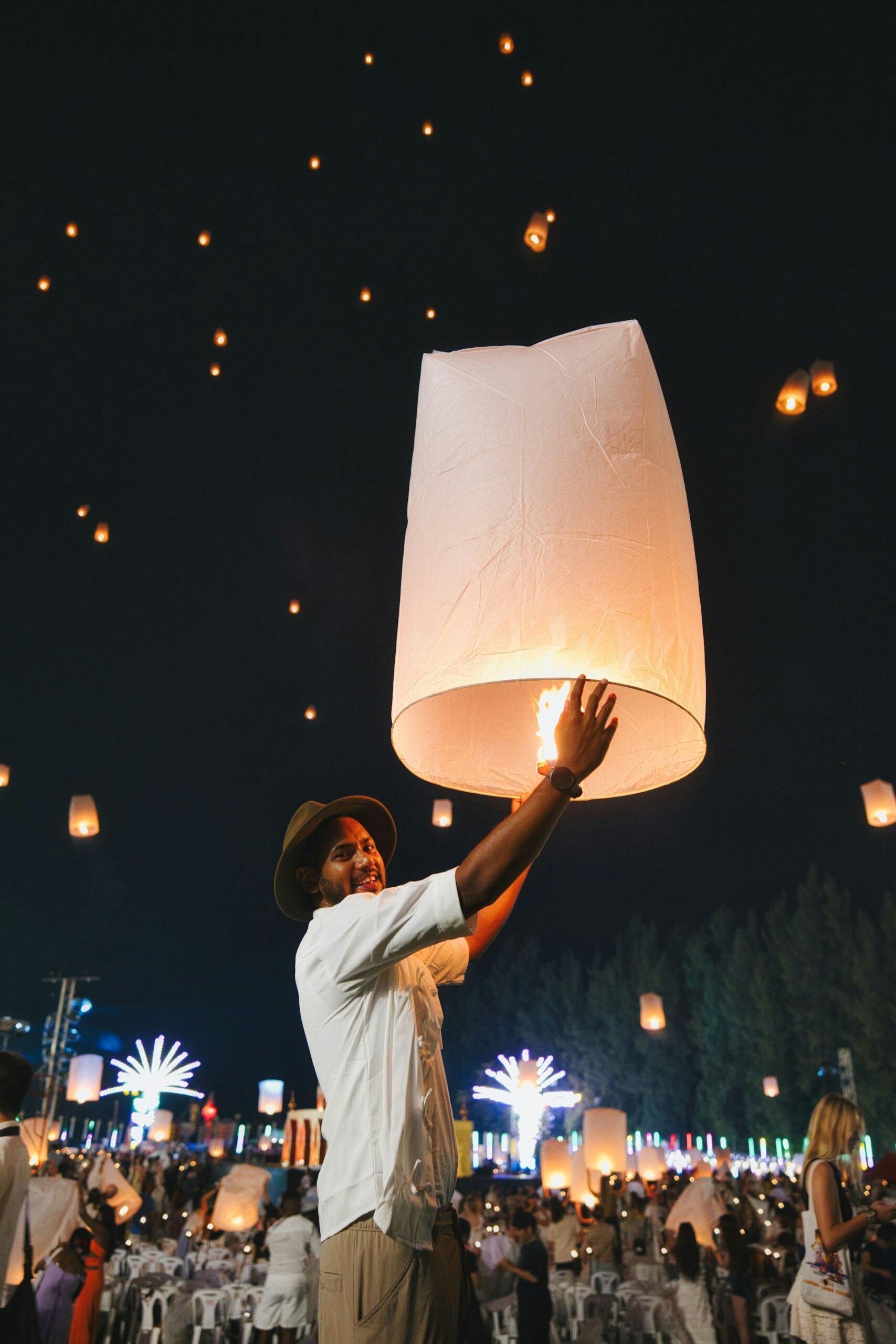 Man releasing a glowing paper sky lantern into the night sky during Yi Peng